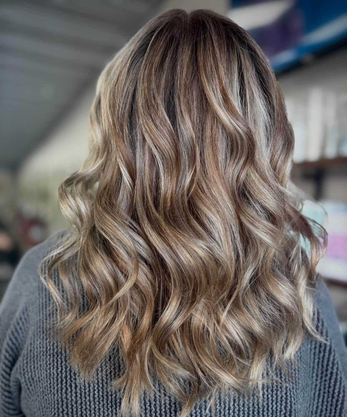 Back view of long wavy hair with blonde highlights on a person wearing a gray knit sweater.