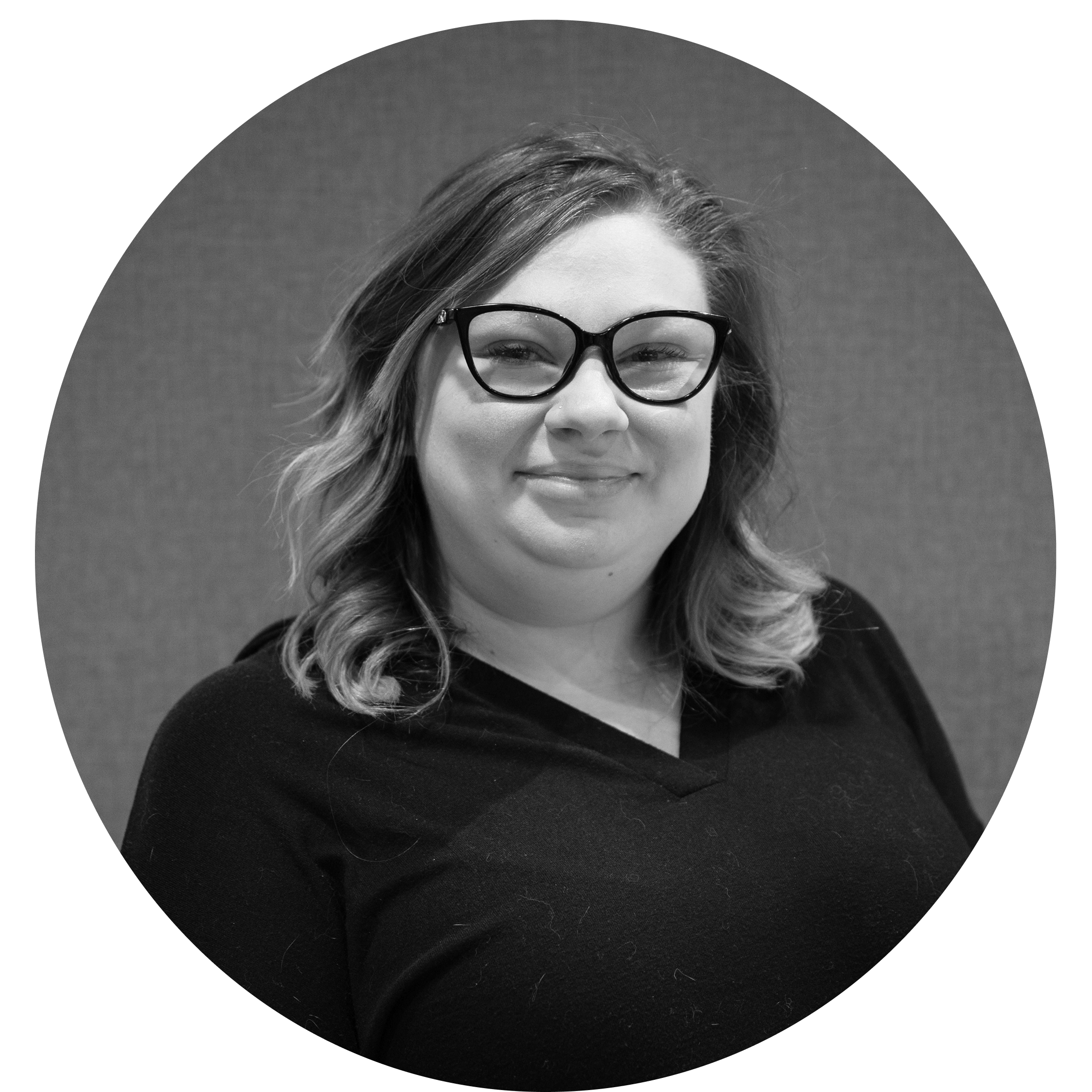 Smiling woman with wavy hair wearing dark-rimmed glasses and a black top, against a plain background.
