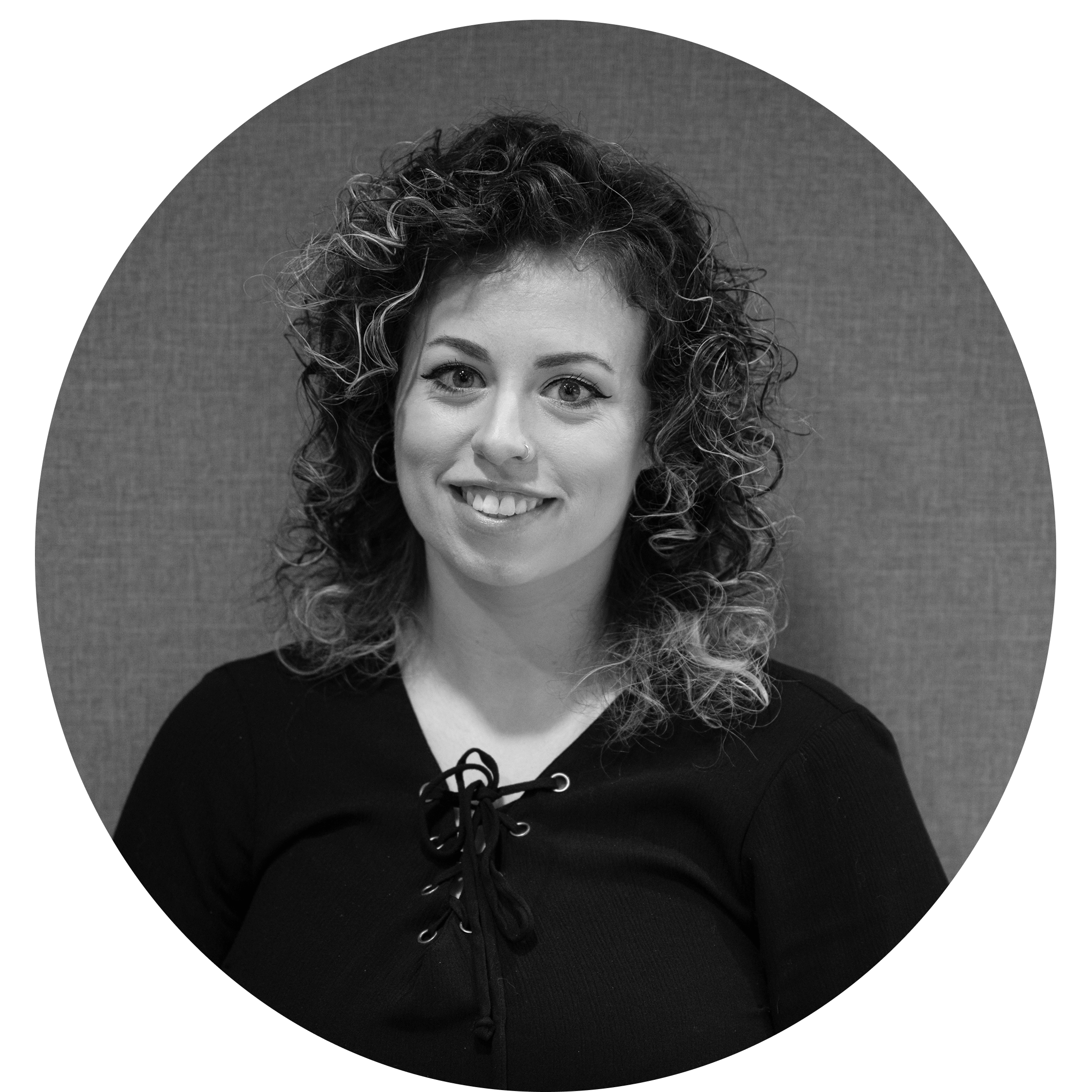 Smiling woman with curly hair wearing a black top with lace-up neckline against a textured background.