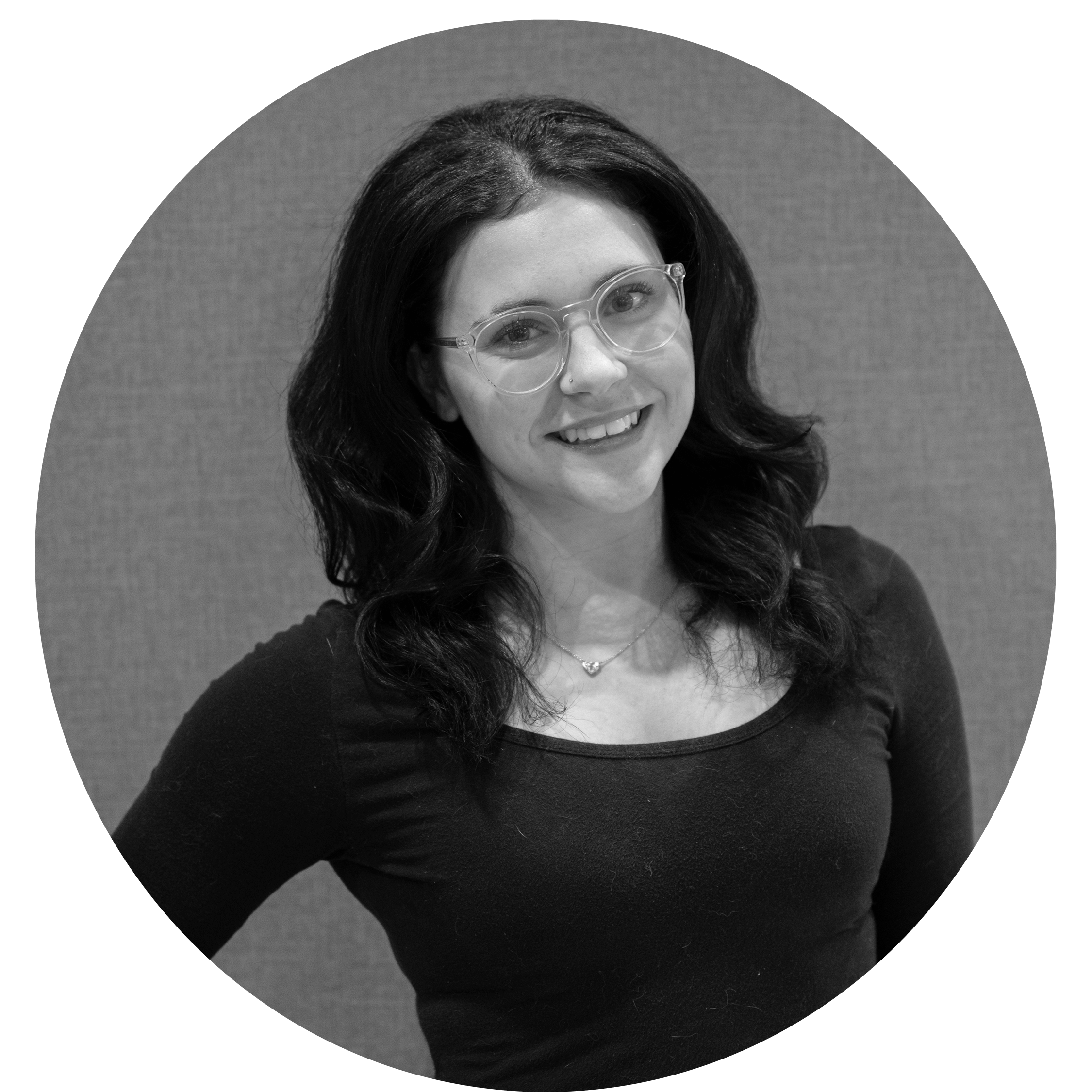 Smiling woman with dark wavy hair, wearing clear glasses, a necklace, and a black top, against a textured background.