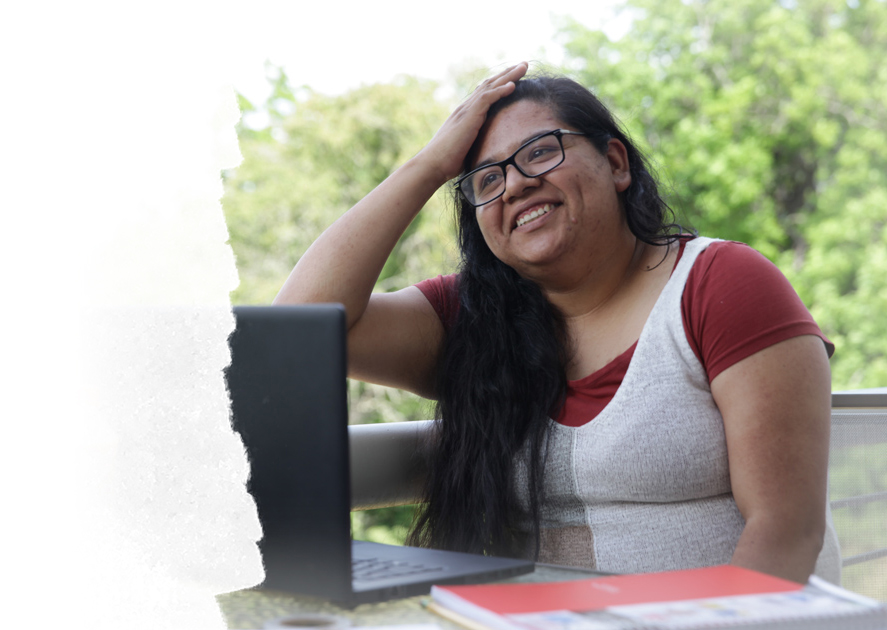 Una estudiante se sienta frente a una computadora con la mano en la cabeza.