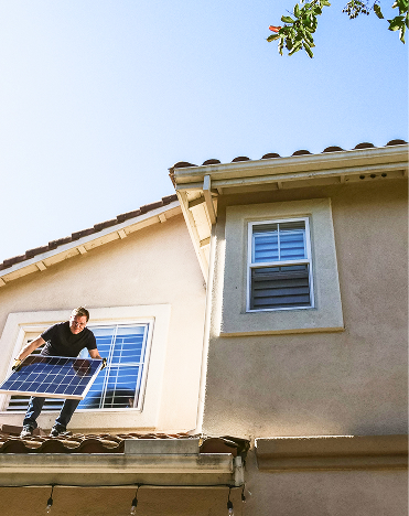 Ein Mann mittleren Alters, der auf seinem Vordach steh und ein PV-Modul in den Händen hält. 