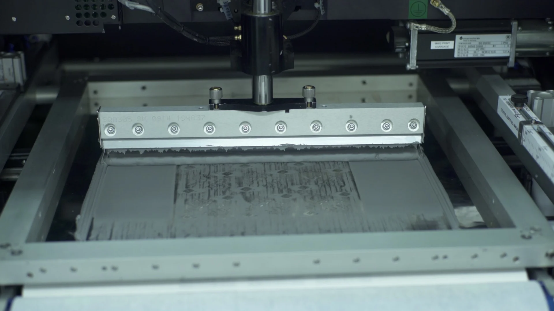 Screen printer squeegee pushing paste across a mesh stencil