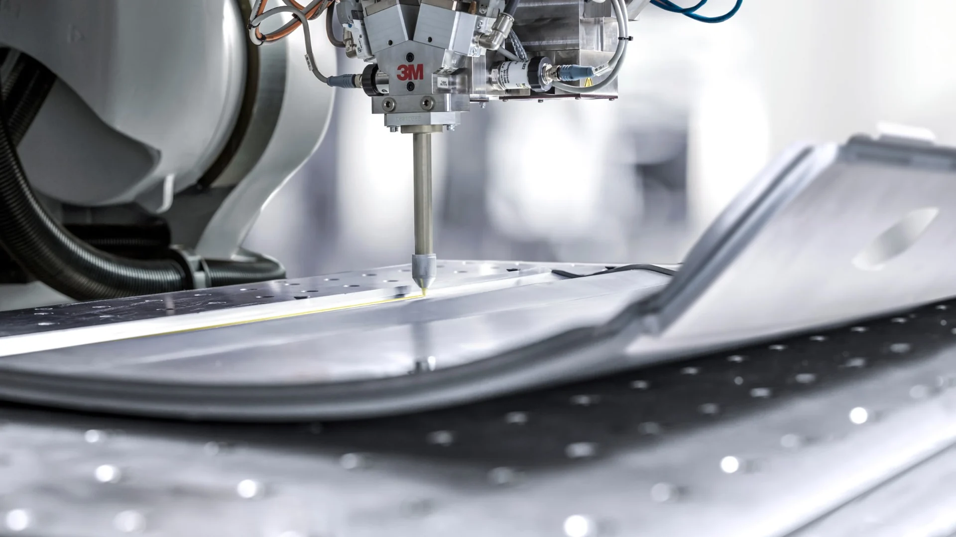 Robotic dispensing head applying an adhesive bead along a metal part