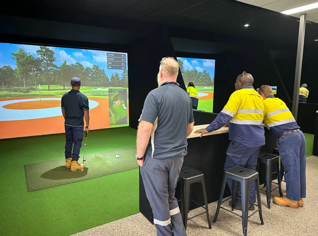 People playing indoor golf simulator at Karratha Indoor Golf with digital course screens and artificial turf