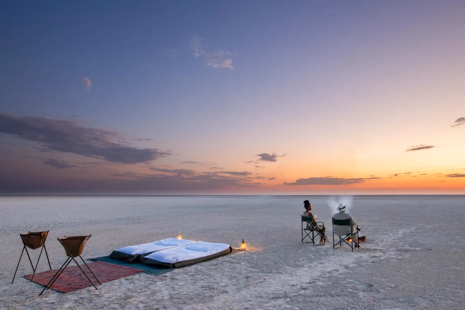 Couple seated in front of fire on large salt pan with bed and small hand basins behind them
