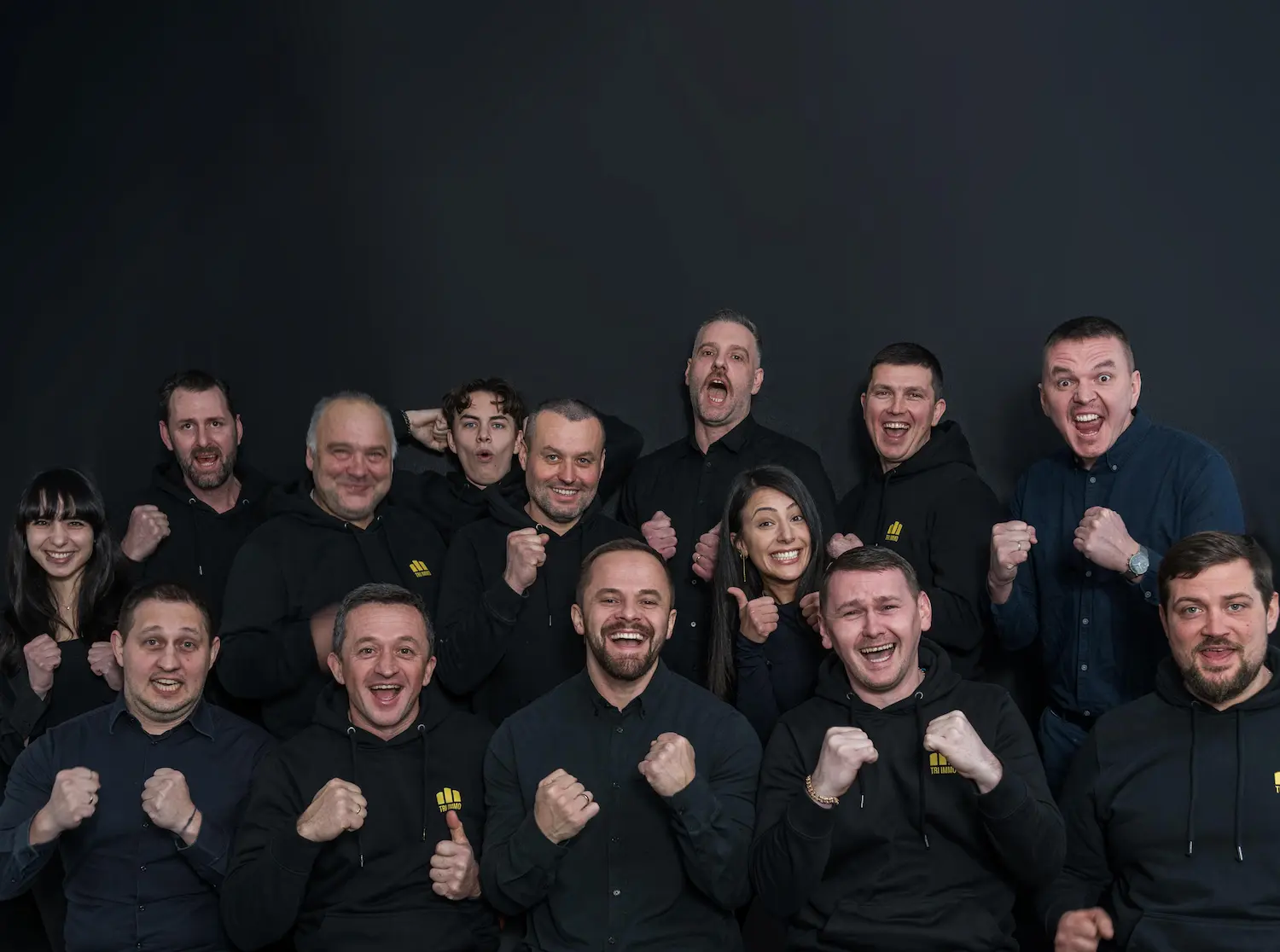 Das Team von TRI IMMO jubelt gemeinsam vor dunklem Hintergrund