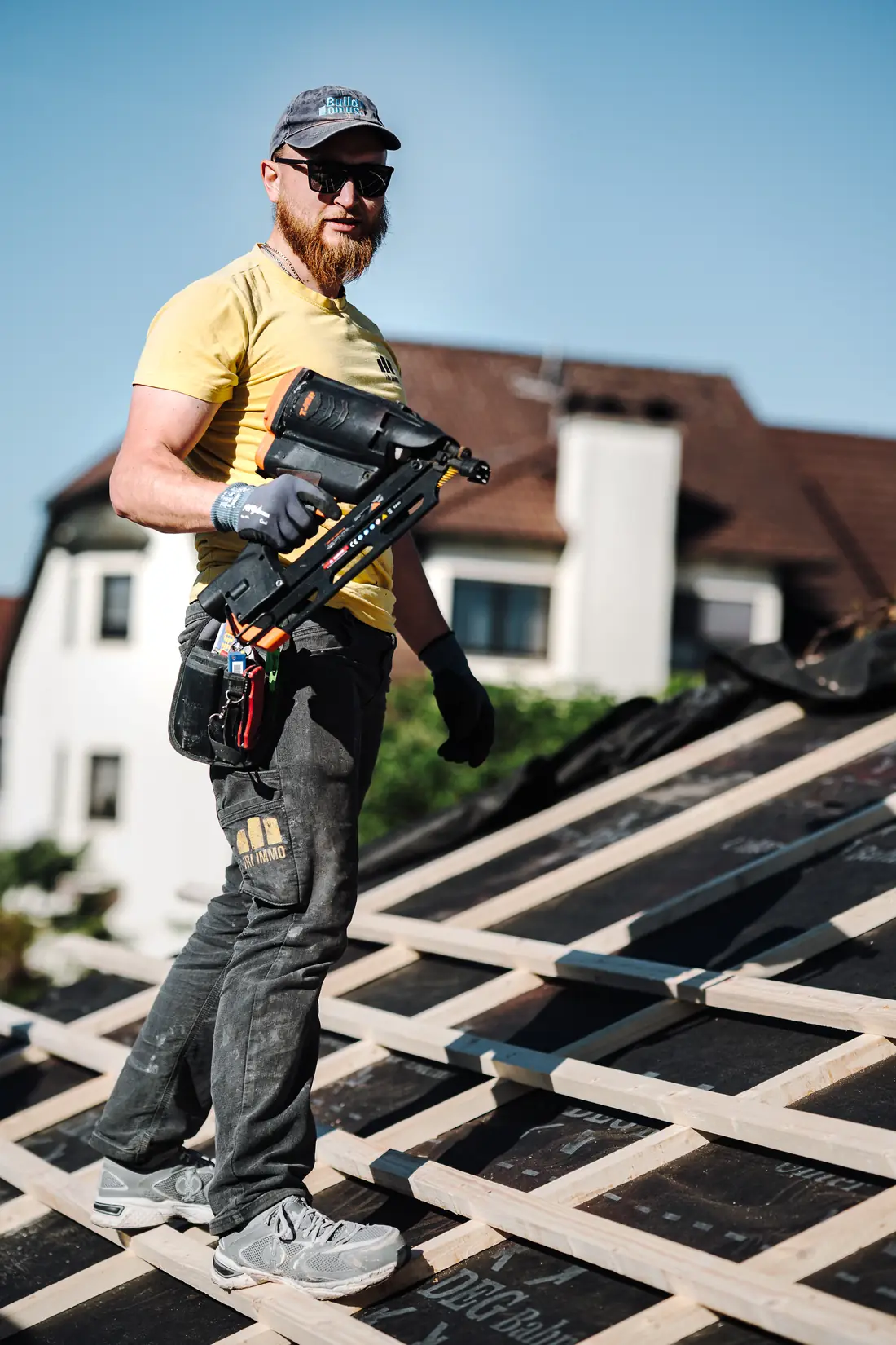 Dachdecker von Bauwerk-Dach mit Druckluftnagler auf einer frisch gelatteten Dachfläche