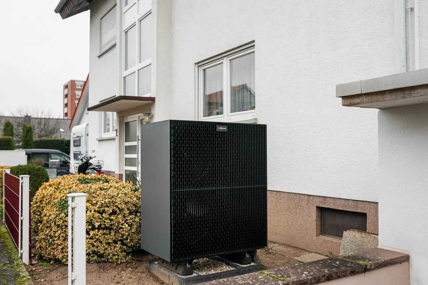 Schwarzes Wärmepumpen-Außengerät vor einem weiß verputzten Wohnhaus