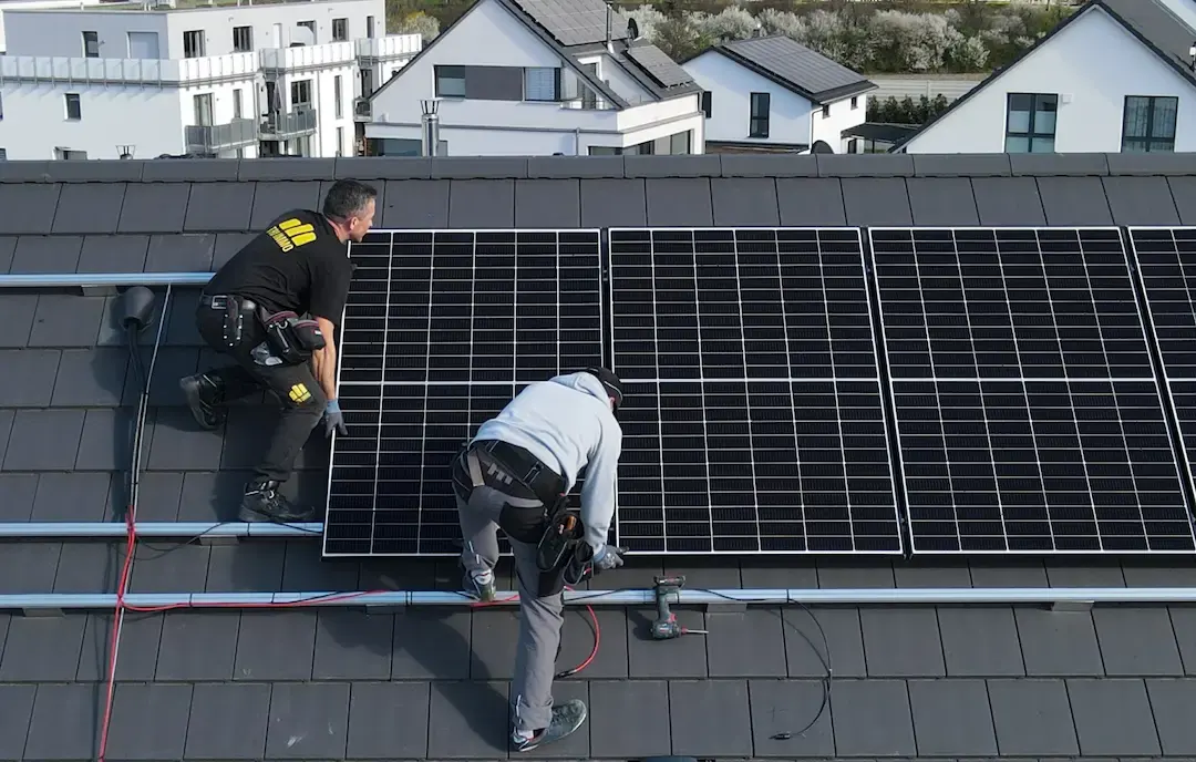Zwei Monteure, einer im TRI-IMMO-Shirt, setzen Photovoltaik-Module auf ein Ziegeldach