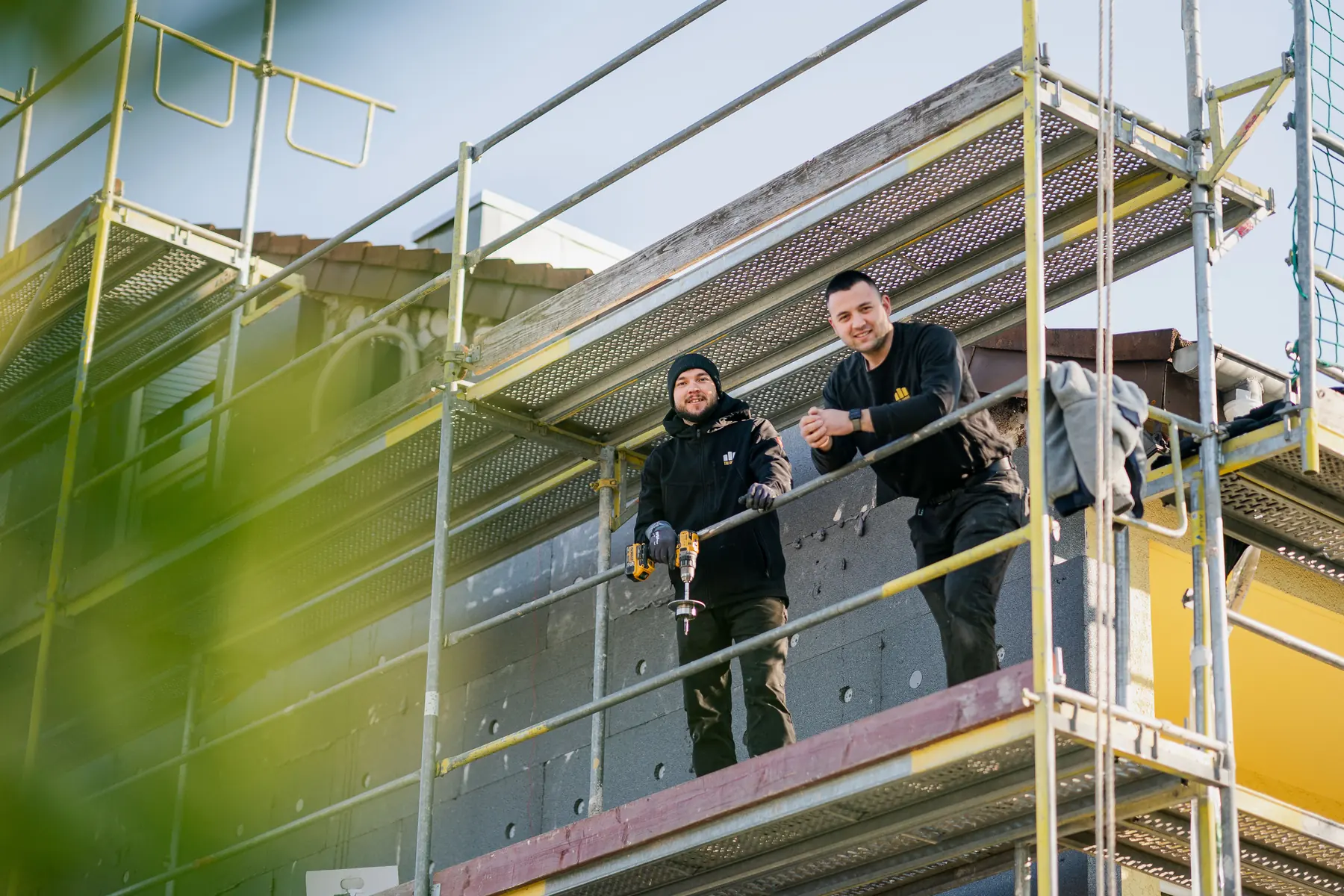 Zwei Mitarbeiter von Bauwerk-Fassade stehen lachend auf dem Gerüst vor einer gedämmten Fassade