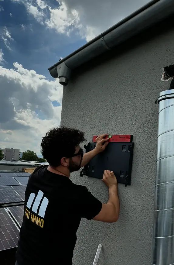 Monteur im TRI-IMMO-Shirt richtet eine Wandhalterung an einer Außenwand mit der Wasserwaage aus