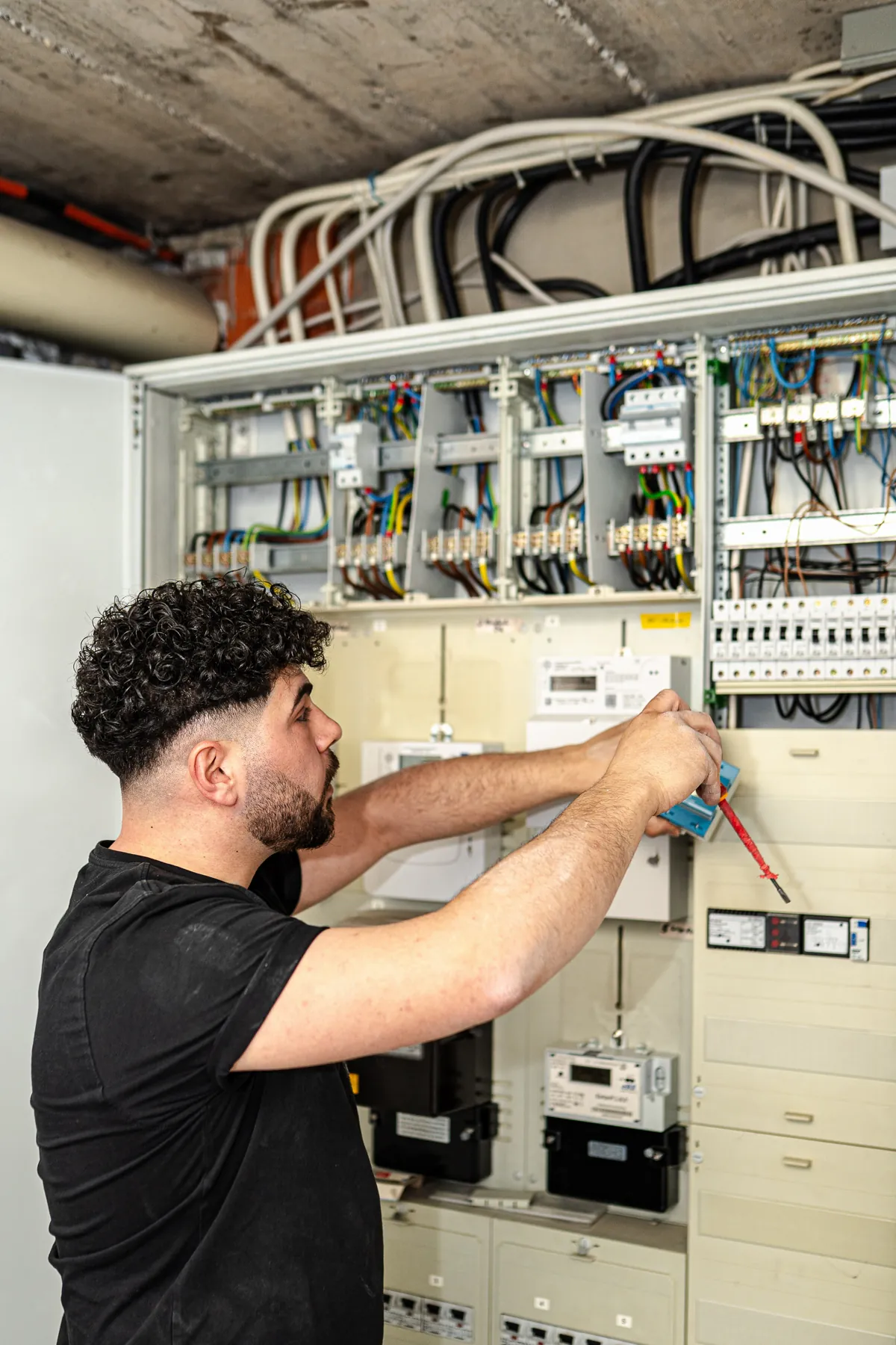 Elektriker im TRI-IMMO-Shirt arbeitet mit Schraubendreher an einem Zählerschrank