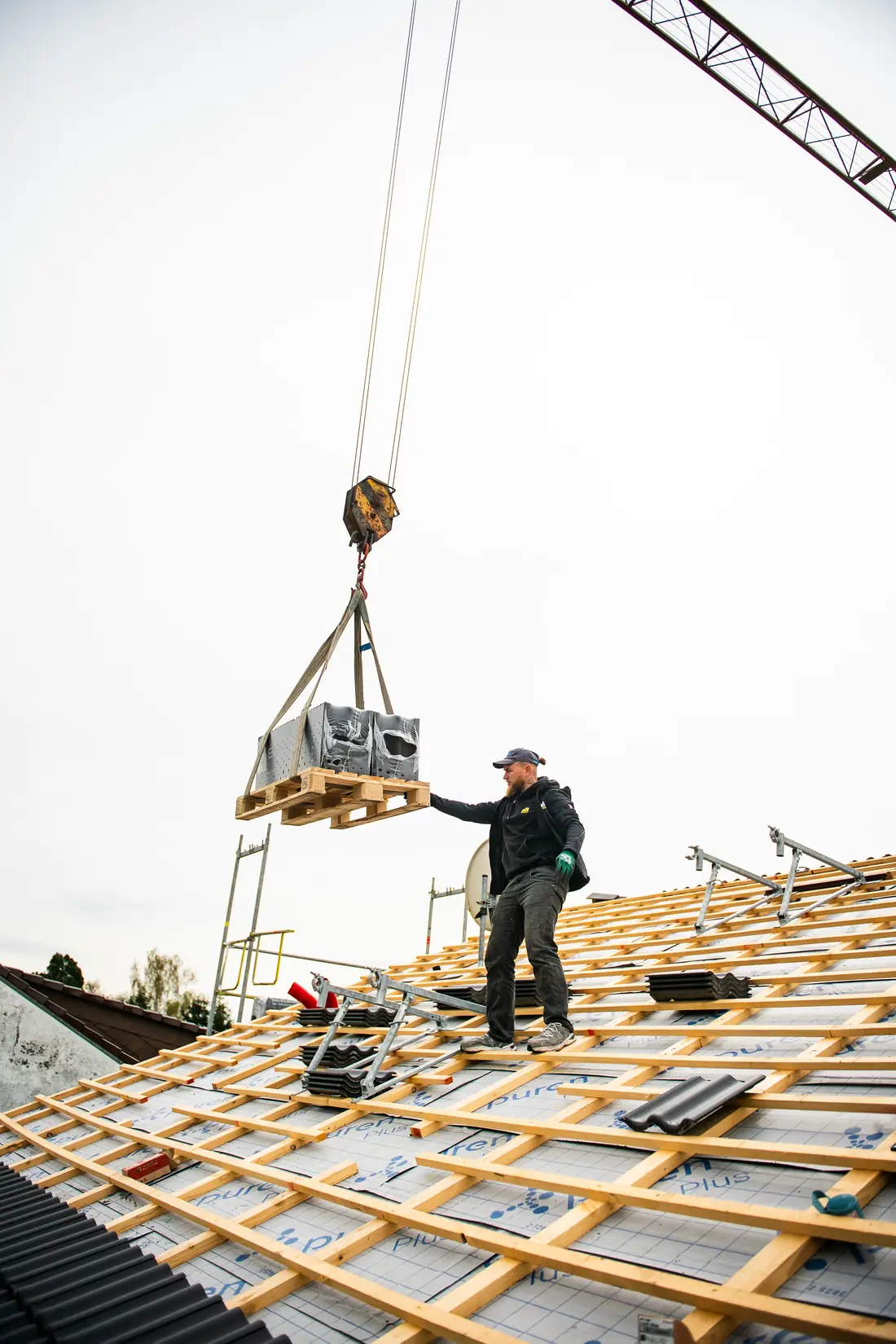 Dachdecker von TRI IMMO nimmt auf einer neu gelatteten Dachfläche Material vom Kran an