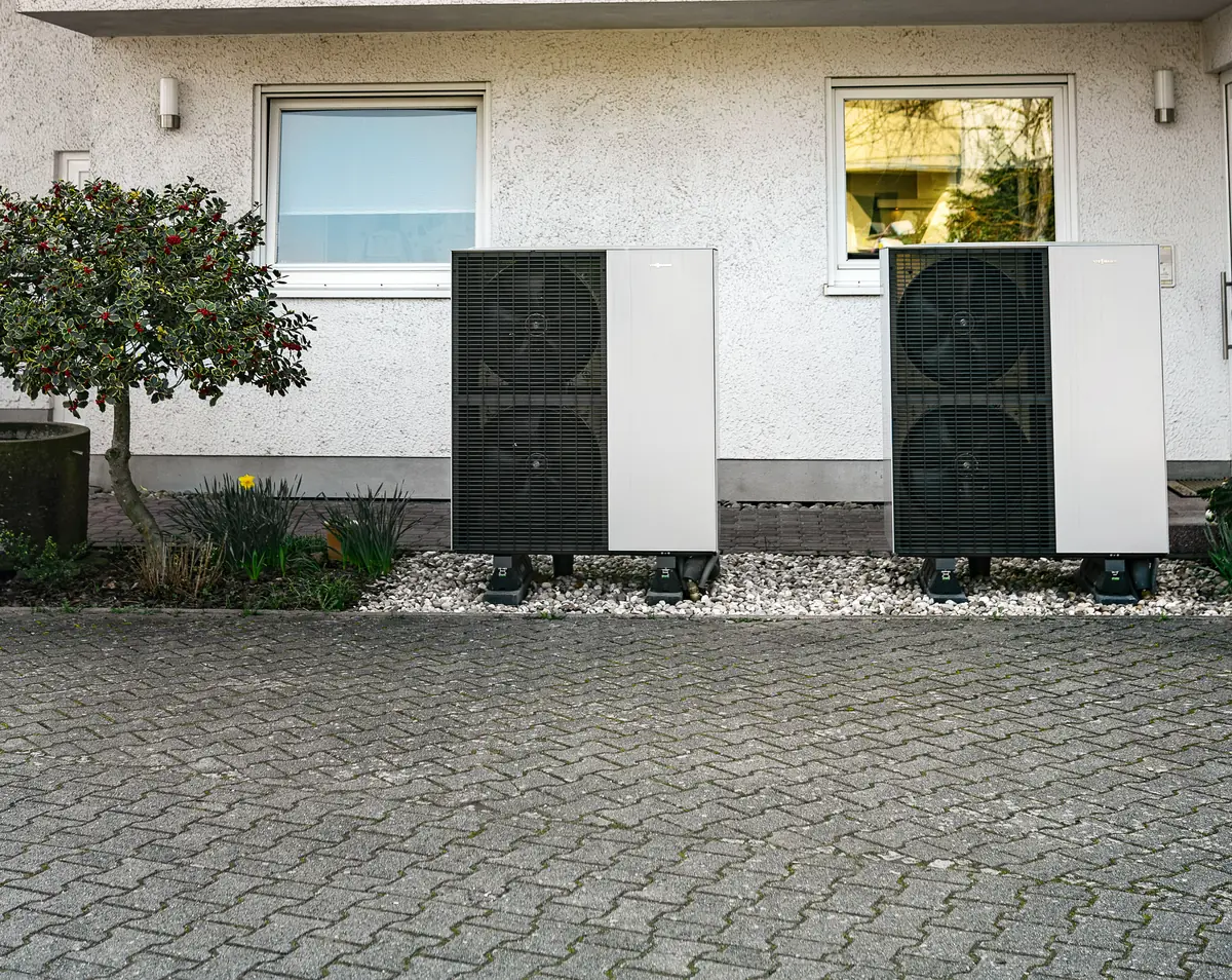 Zwei Wärmepumpen-Außengeräte auf ihrem Fundament vor einem frisch verputzten Wohnhaus