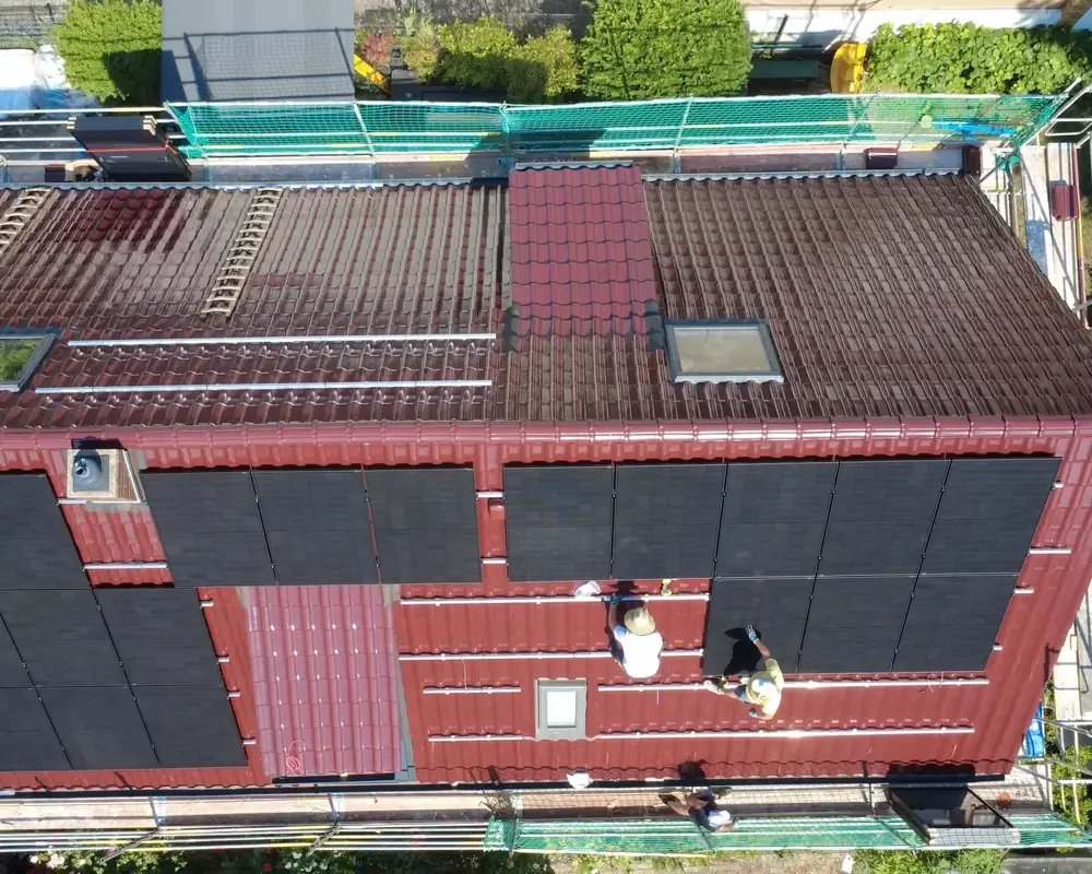 Drohnenbild aus Mannheim-Feudenheim: neues Dach mit roten Tonziegeln, zwei Monteure setzen die Photovoltaikmodule