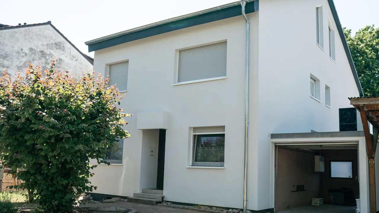 Fertig sanierte Straßenseite eines Einfamilienhauses: weiße, gedämmte Fassade, neue Fensterbänke, daneben Garage und Carport