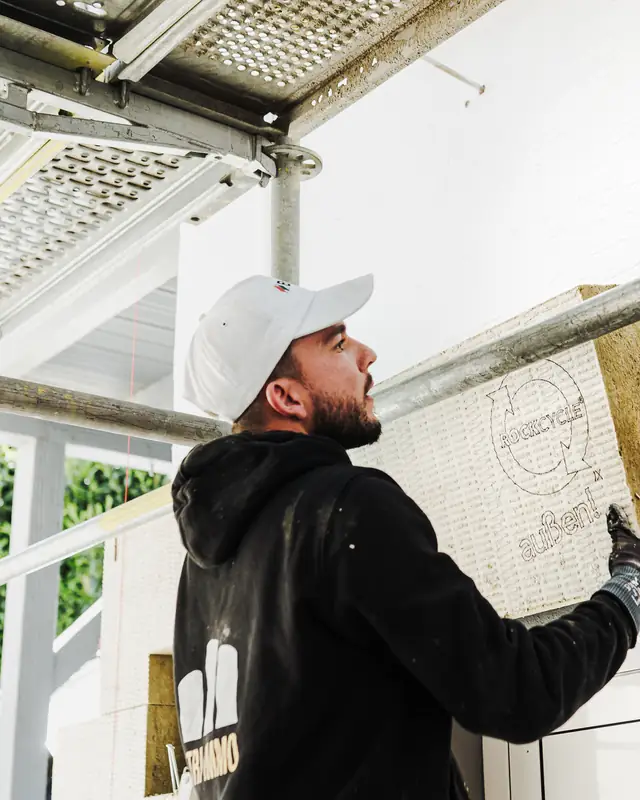 Fassadenmonteur setzt eine Dämmplatte aus Mineralwolle an die Wand, über ihm das Gerüst
