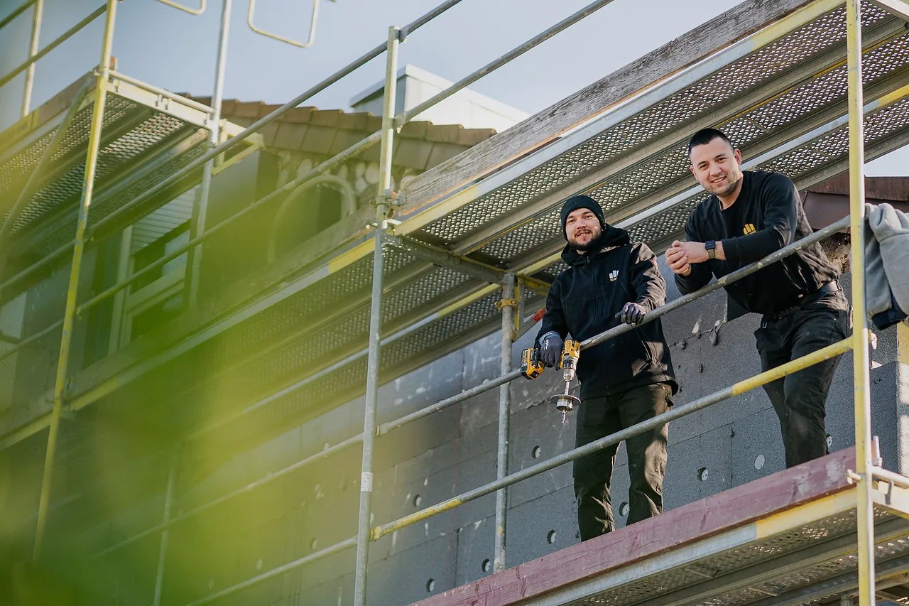 Fassadensanierung: Zwei Fassadenmonteure auf dem Gerüst, hinter ihnen die neuen grauen Dämmplatten an der Hauswand