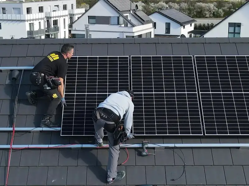 Zwei Monteure setzen schwarze Photovoltaikmodule auf ein Ziegeldach