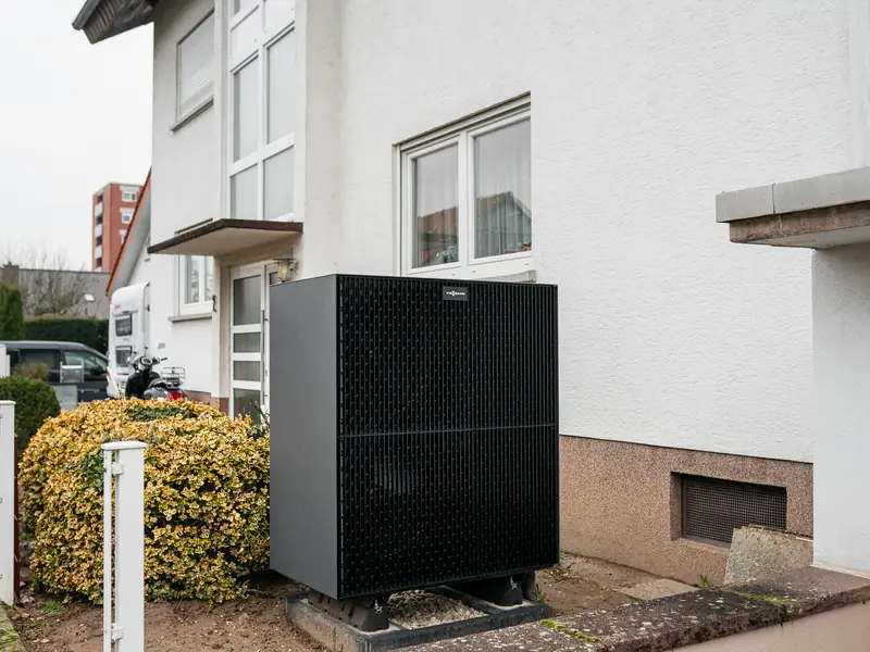 Außengerät einer Wärmepumpe vor einem hellen Wohnhaus