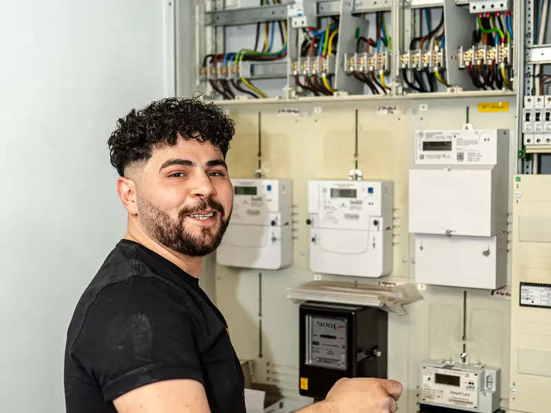 Elektriker arbeitet lächelnd am Zählerplatz eines Hauses