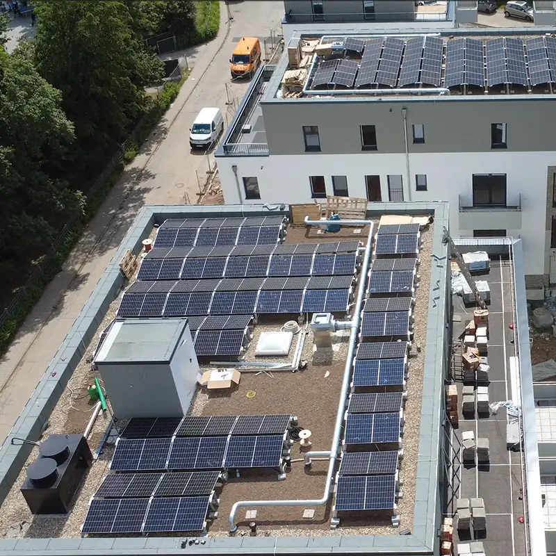 Dasselbe Flachdach danach, schräg von oben: Reihen aufgeständerter Photovoltaikmodule, dahinter ein weiteres Haus mit Modulen