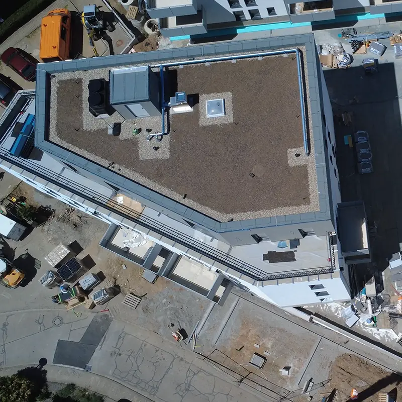 Neubau in Heppenheim von oben vor der Montage: leeres Flachdach mit Kies und Substrat, daneben die Baustelle