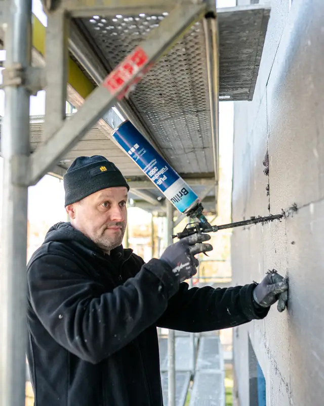Handwerker arbeitet auf dem Gerüst mit einer Schaumpistole an der Fassadendämmung