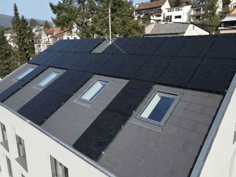 Schwarze Photovoltaikmodule und Dachfenster auf dem neu gedeckten Dach eines Mehrfamilienhauses