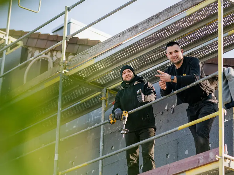 Zwei Handwerker auf dem Gerüst vor frisch angebrachten grauen Dämmplatten