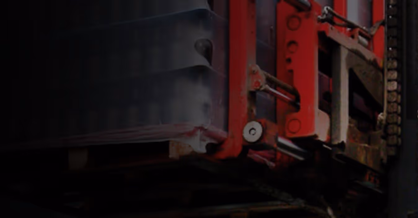 A pallet jack lifting stacked packages in a dimly lit industrial setting.