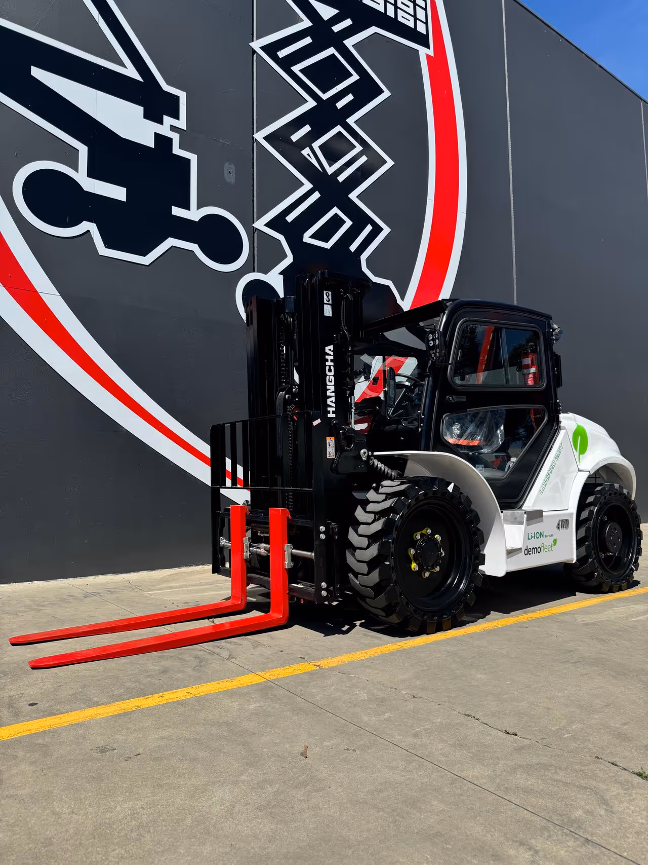 A forklift with red forks is parked in a lot next to a large wall mural.