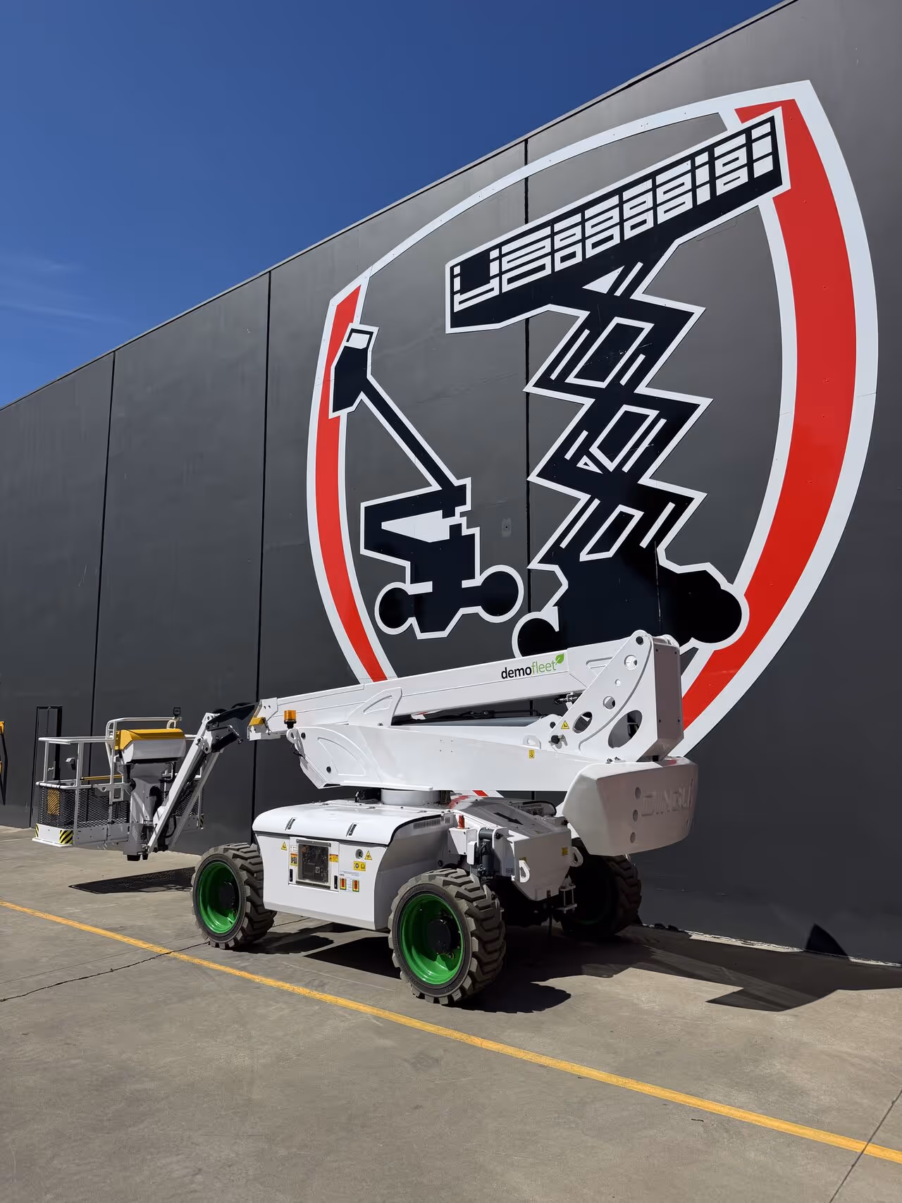 A white scissor lift with green wheels is parked in front of a large wall mural.