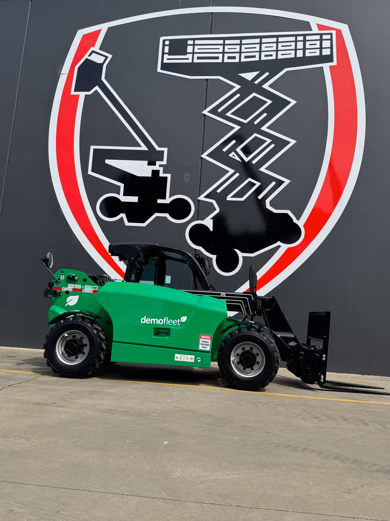 A green forklift is parked in front of a large logo on a gray wall.