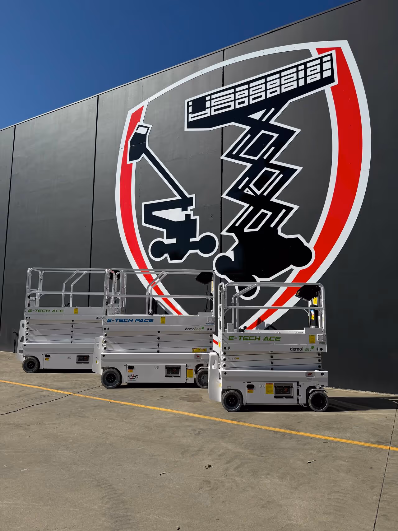 Three white mobile scissor lifts positioned in front of a large wall mural.