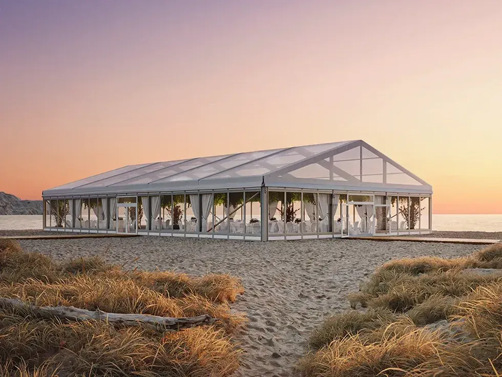 Elegant evenemangstält nära havet, omgivet av strandgräs.