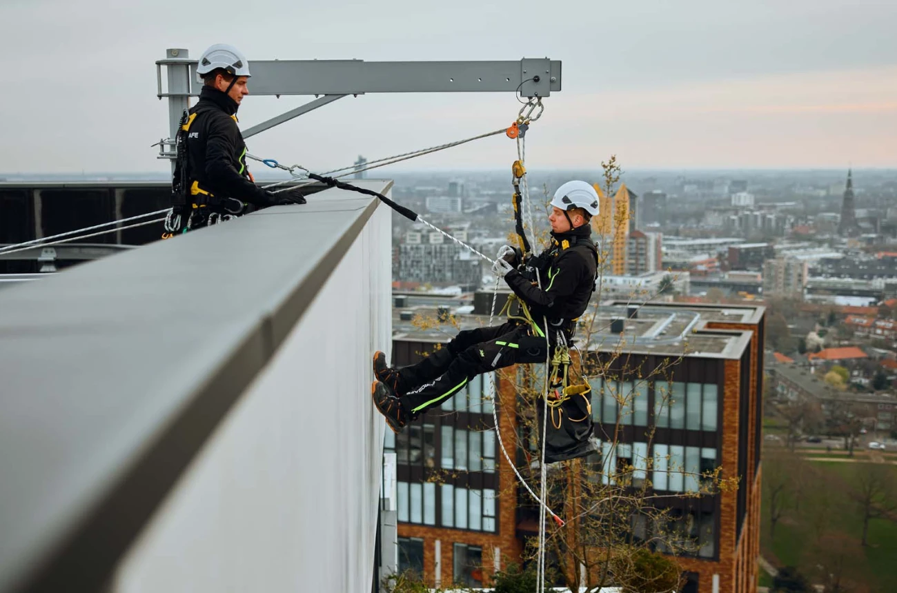 een persoon hangt in touwen van een gebouw op hoogte met een harnas om