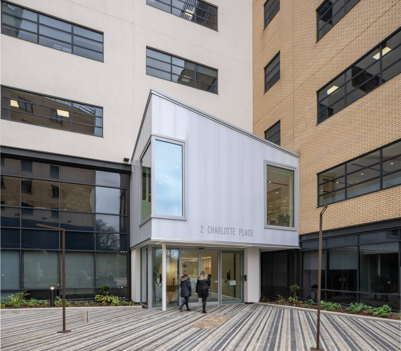 Modern building entrance with glass doors at 2 Charlotte Place, two people walking towards the entrance.