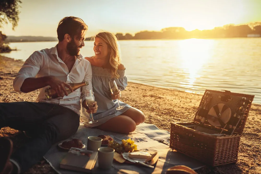 Romantic couple enjoying sunset picnic with champagne by the lake