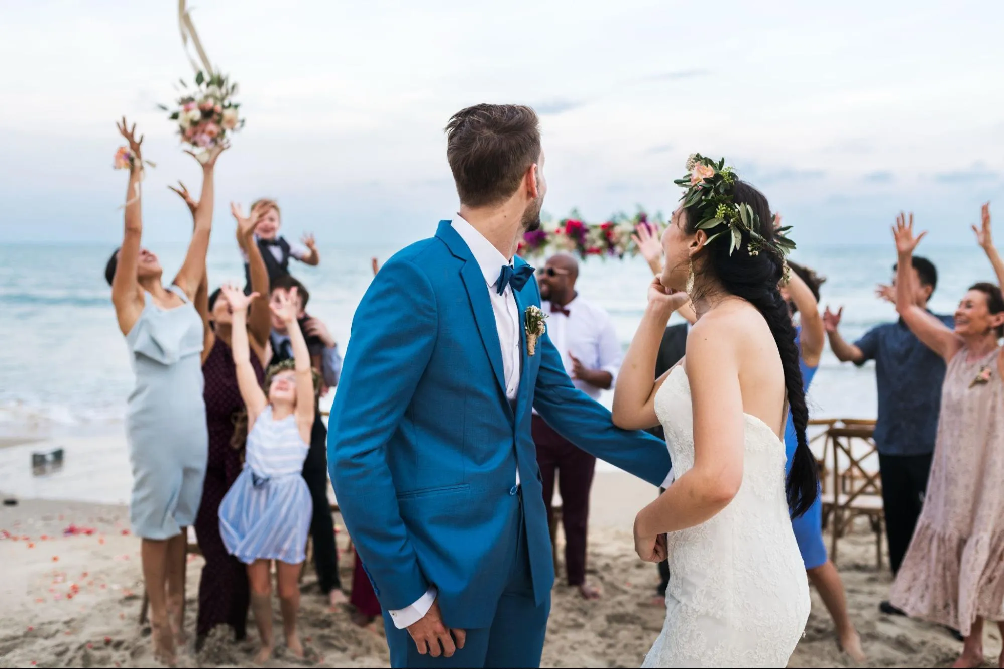Bride and groom in wedding attire celebrating with guests at a beach wedding by the sea