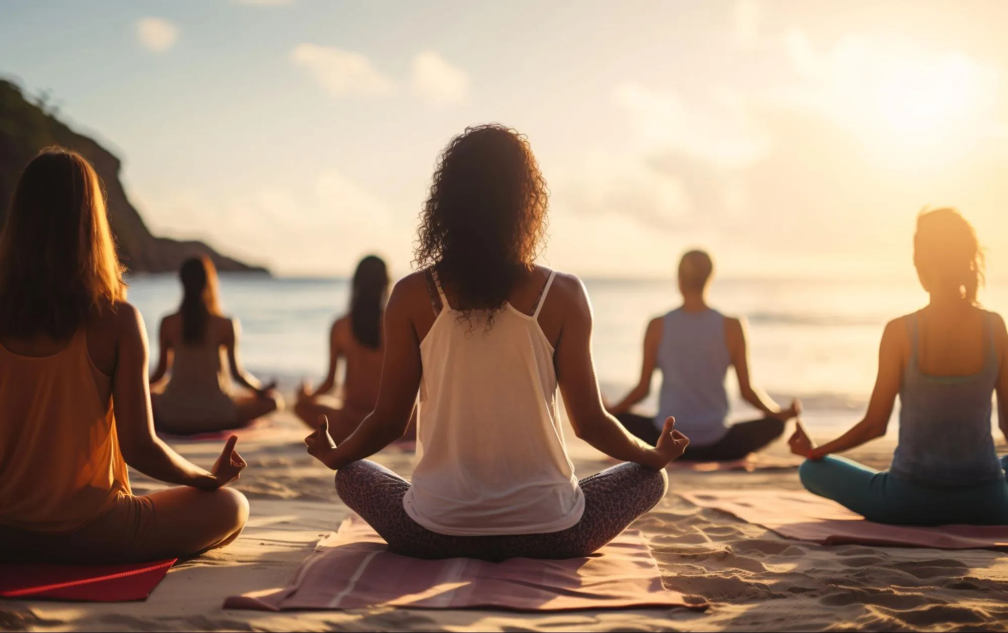 Group of people practicing yoga meditation on the beach at sunrise with ocean view