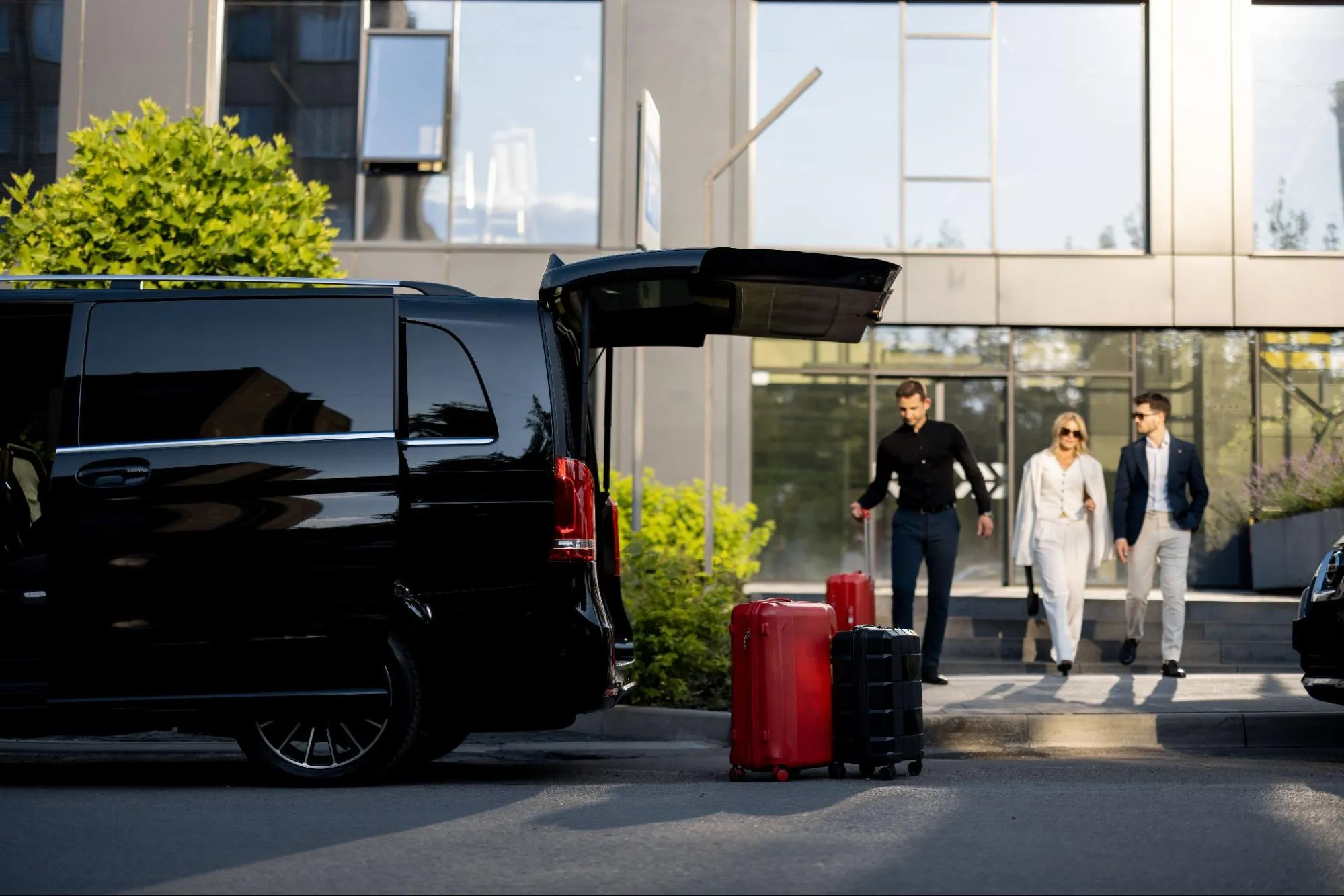 Luxury airport transfer with black van and suitcases as business travelers walk from hotel