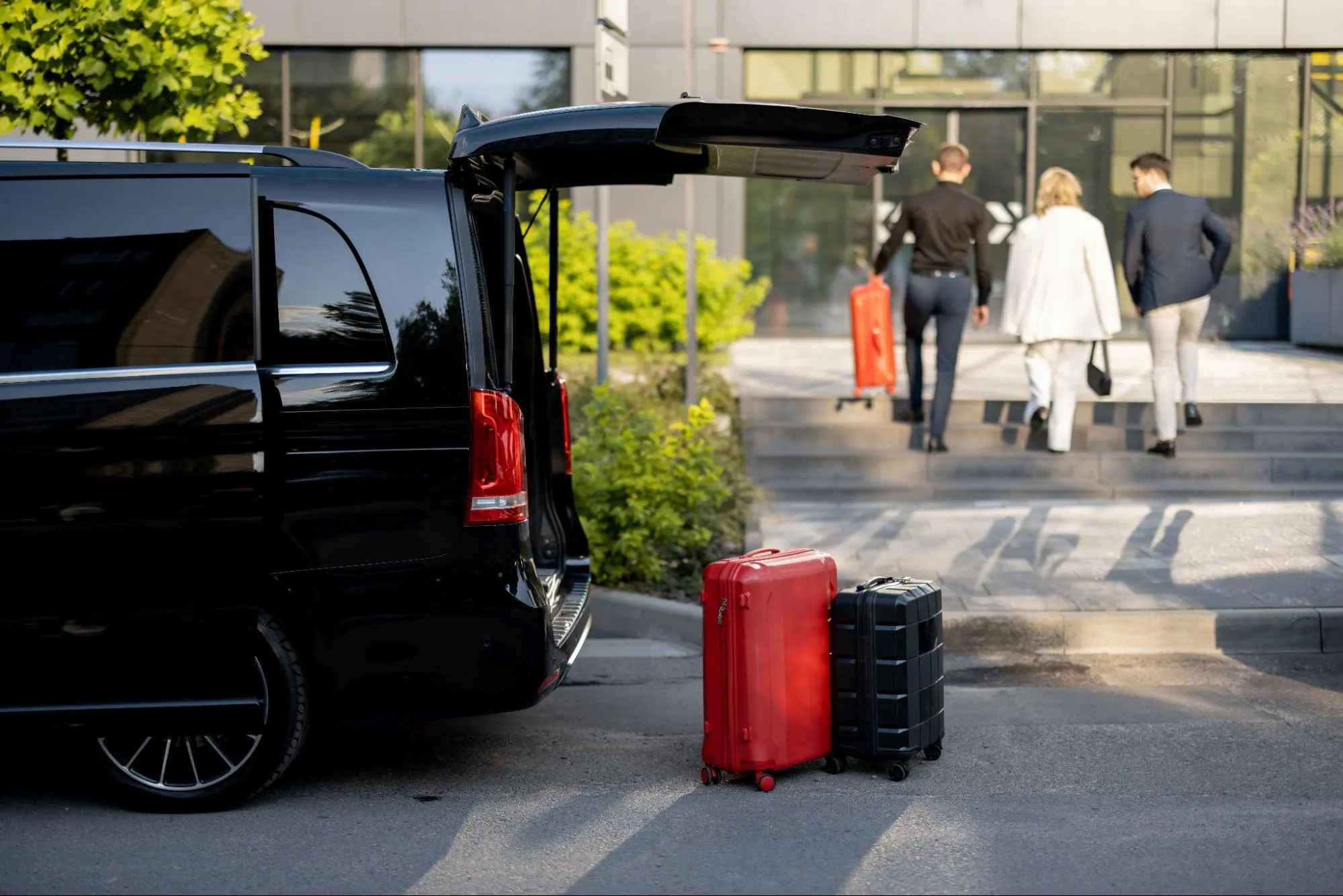Black luxury van with suitcases outside hotel as business travelers depart with luggage