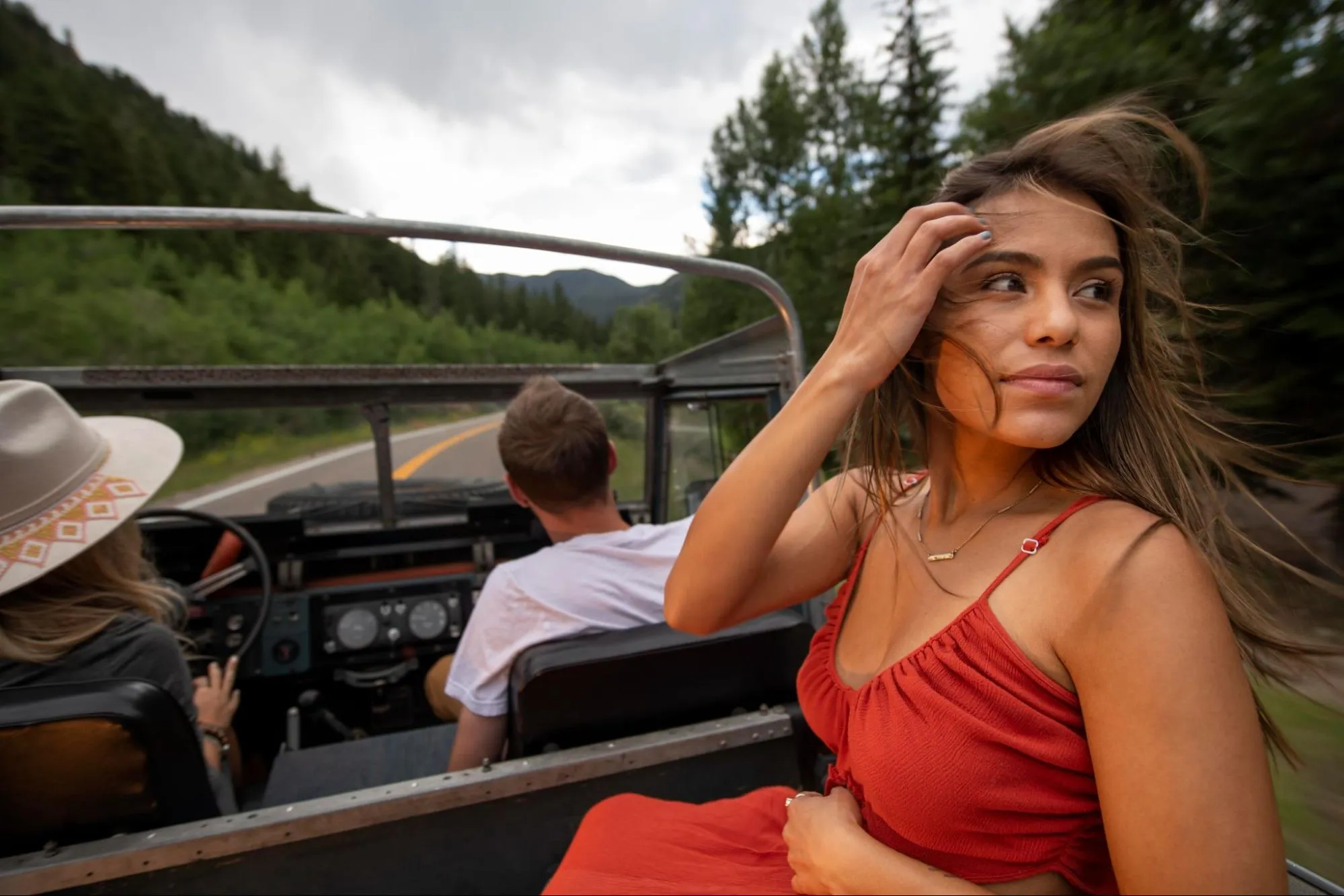 Young woman enjoying road trip in open-top jeep through scenic mountain forest