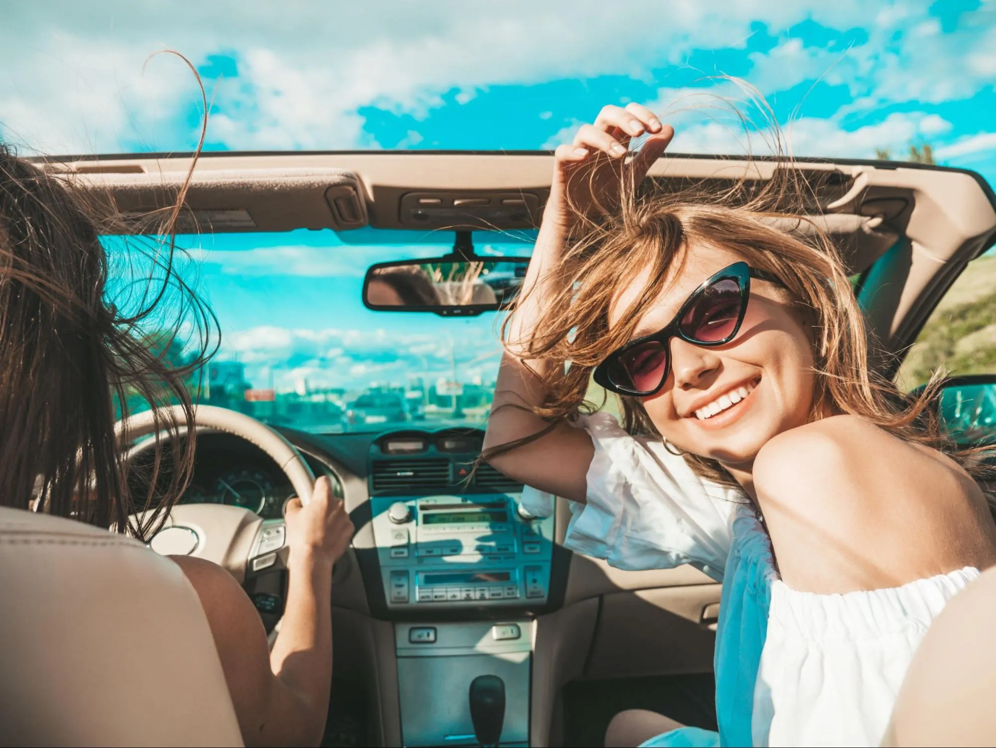 Happy young woman wearing sunglasses enjoying a road trip in a convertible car on a sunny day