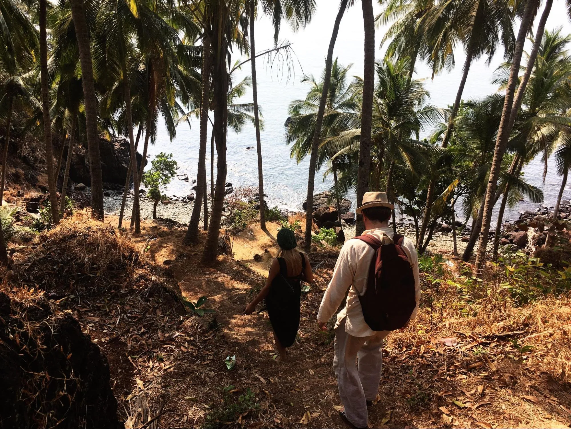 Couple hiking down tropical trail through palm trees towards the ocean
