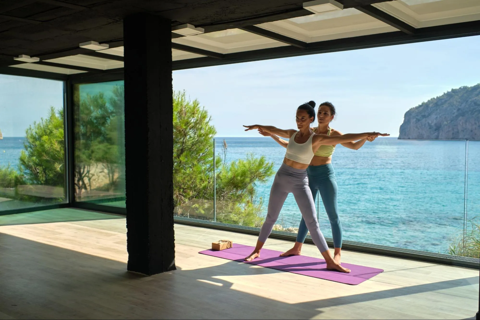 Yoga instructor guiding student in pose during beachfront yoga class with ocean view