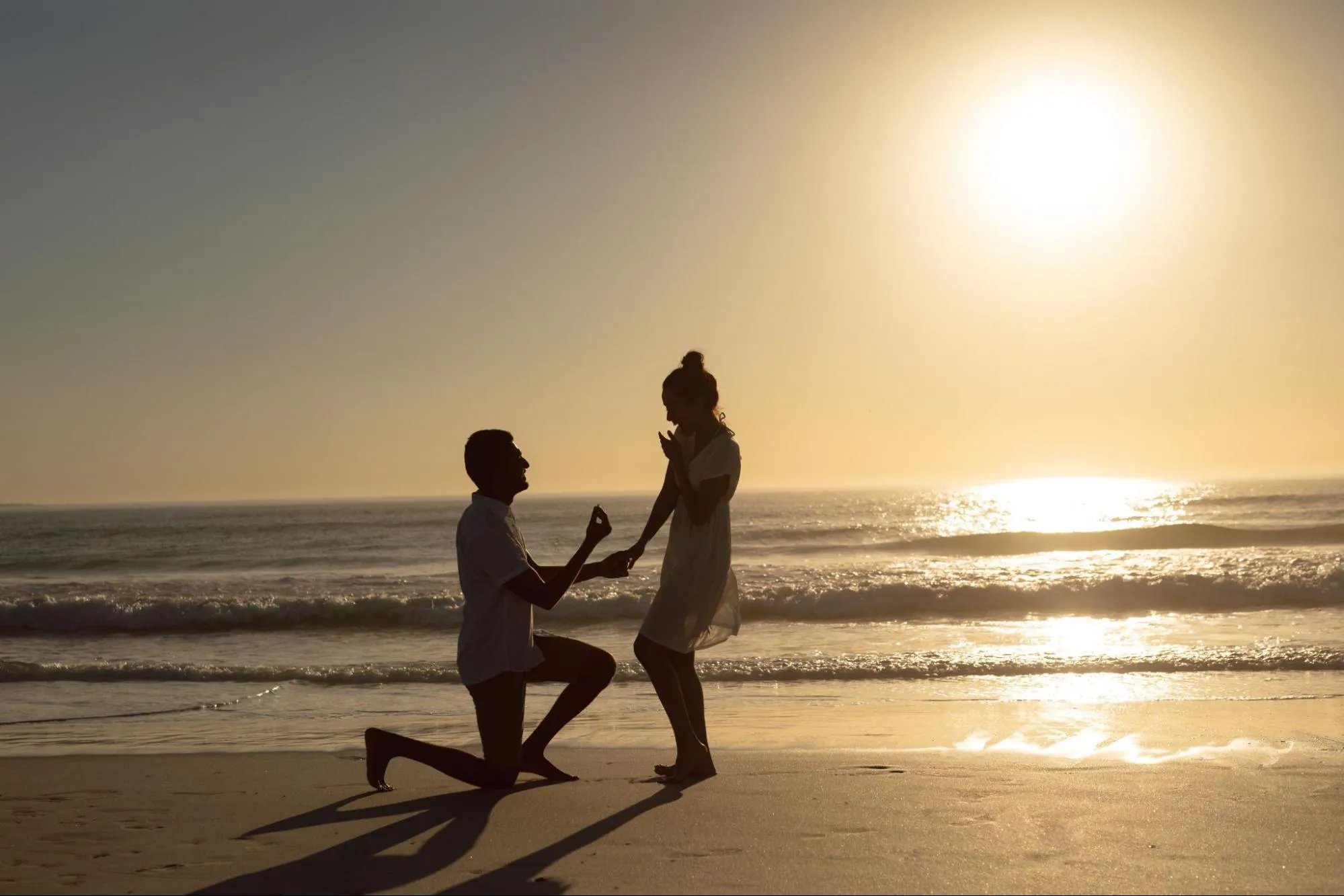 Man proposing to woman on the beach at sunset with engagement ring