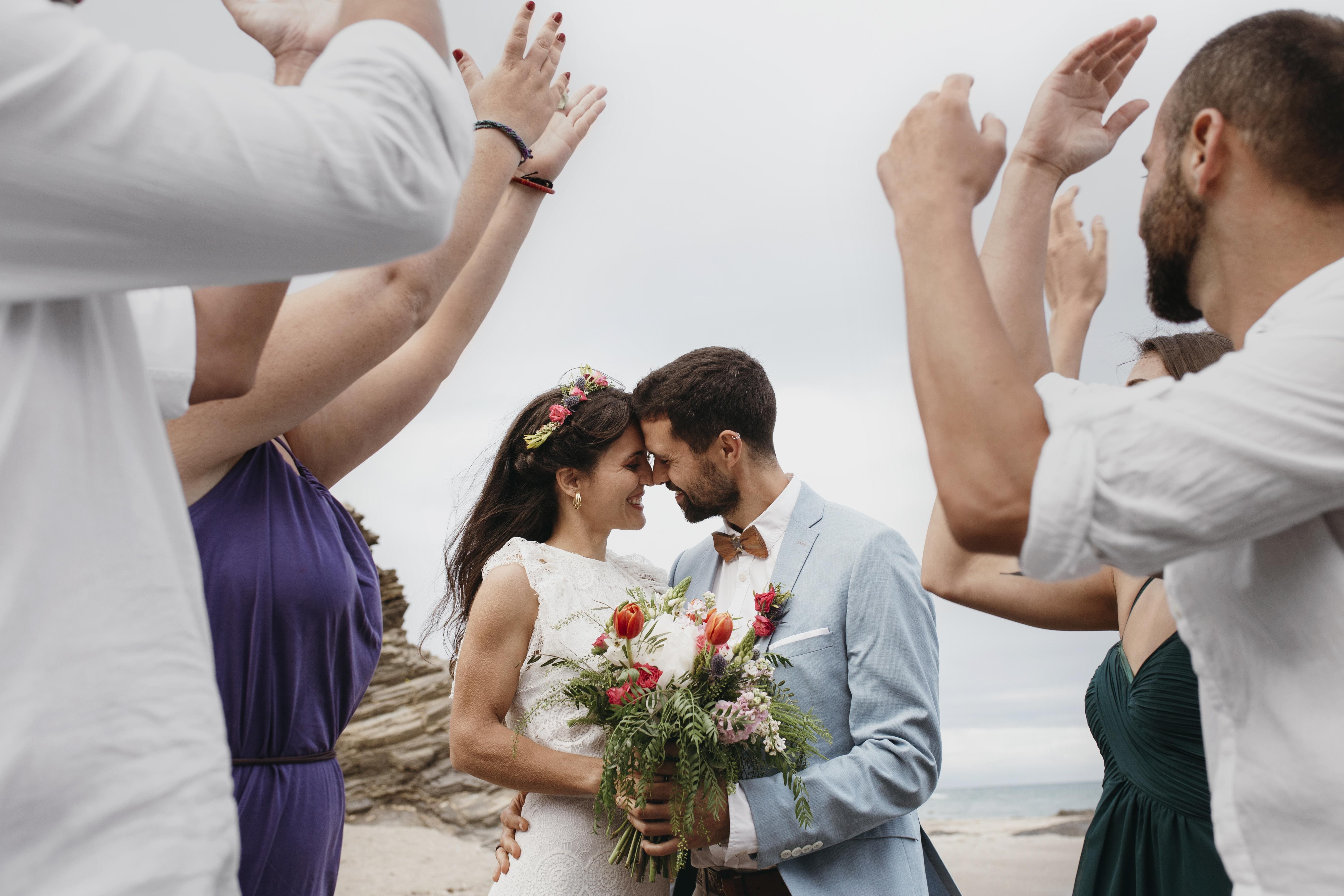 Bride and groom smiling and touching foreheads as friends raise their hands in celebration during a beach wedding in the Dominican Republic.
